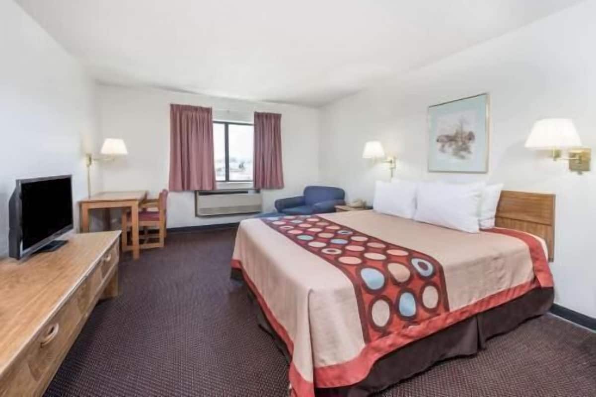 A hotel room with a bed, a desk, a chair, a TV, and a window with curtains.
