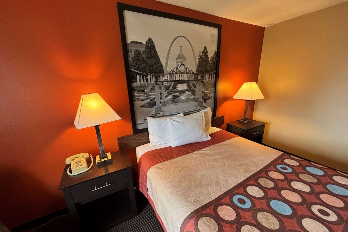 A hotel room with a bed, two bedside lamps, a telephone, and a framed picture of a bridge and dome.