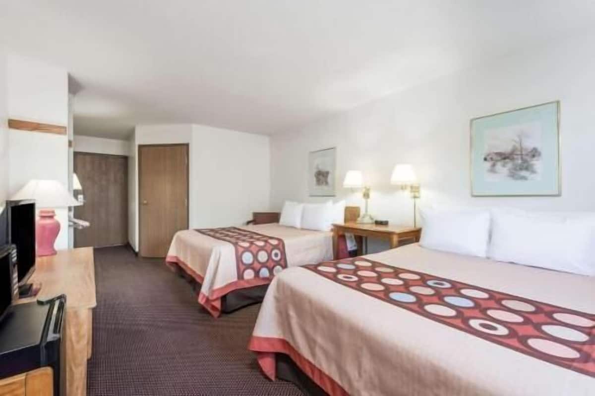 A hotel room with two beds, a desk, a chair, a television, and a door.