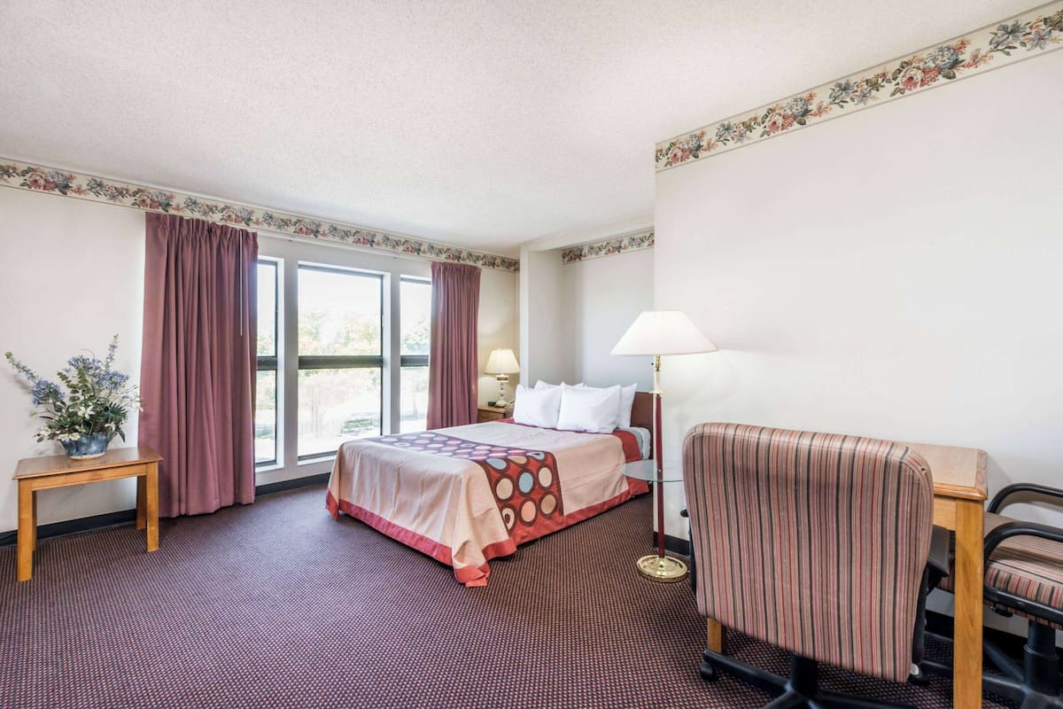 A hotel room with a bed, a desk, a chair, a lamp, and a window with curtains.