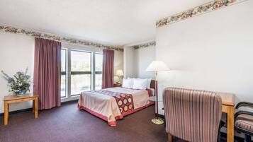 A hotel room with a bed, a desk, a chair, a lamp, and a window with curtains.