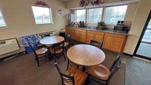 Una cocina pequeña y acogedora con una mesa redonda y cuatro sillas, armarios de madera, un microondas y una cafetera.
