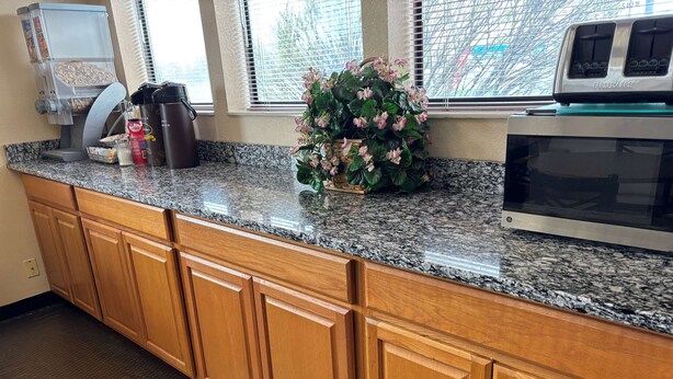 Una cocina con encimeras de granito, gabinetes de madera, cafetera, microondas y una planta en maceta.