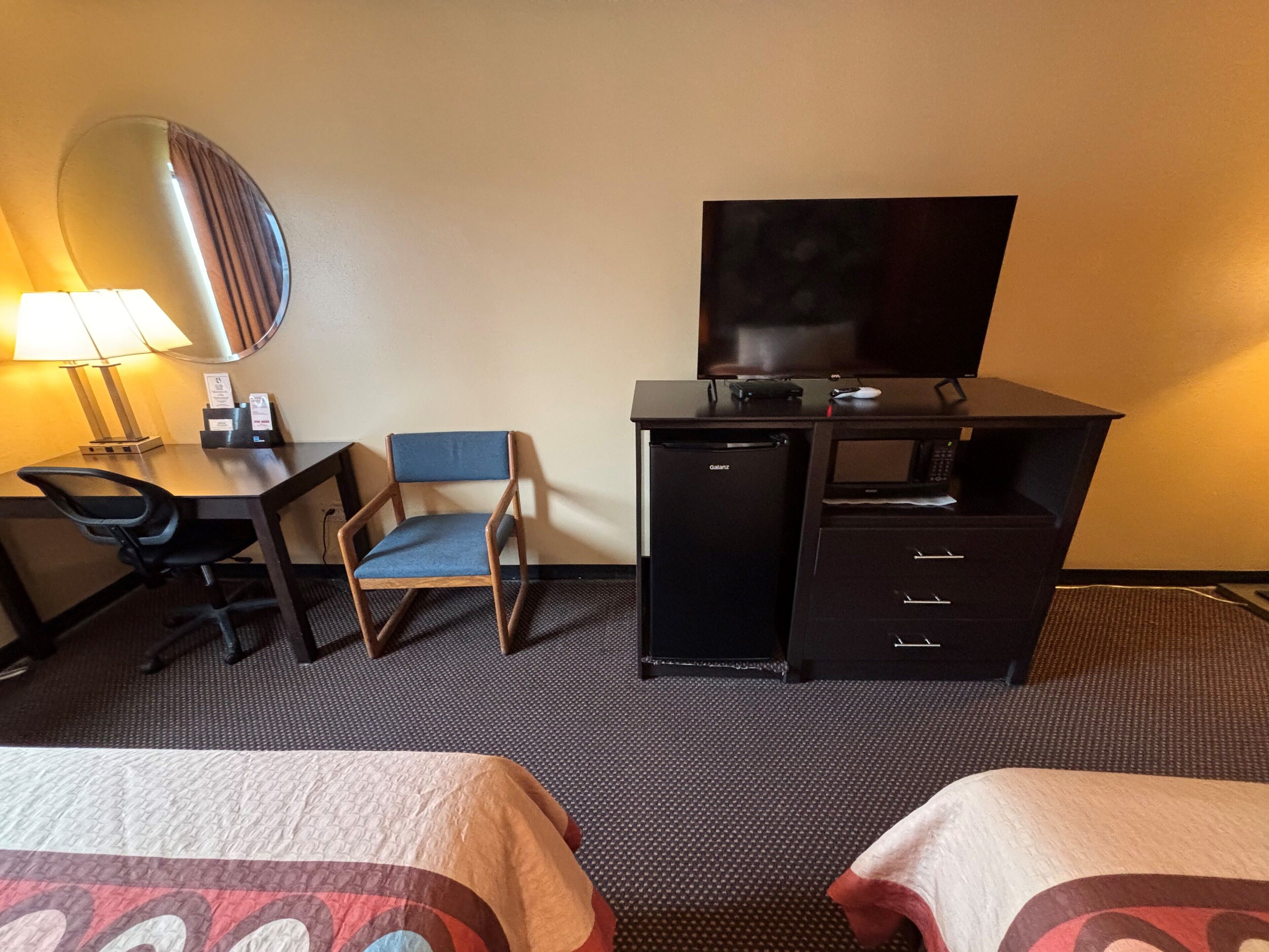 Ett hotellrum med ett skrivbord, en stol, en tv, en minibar och två sängar.