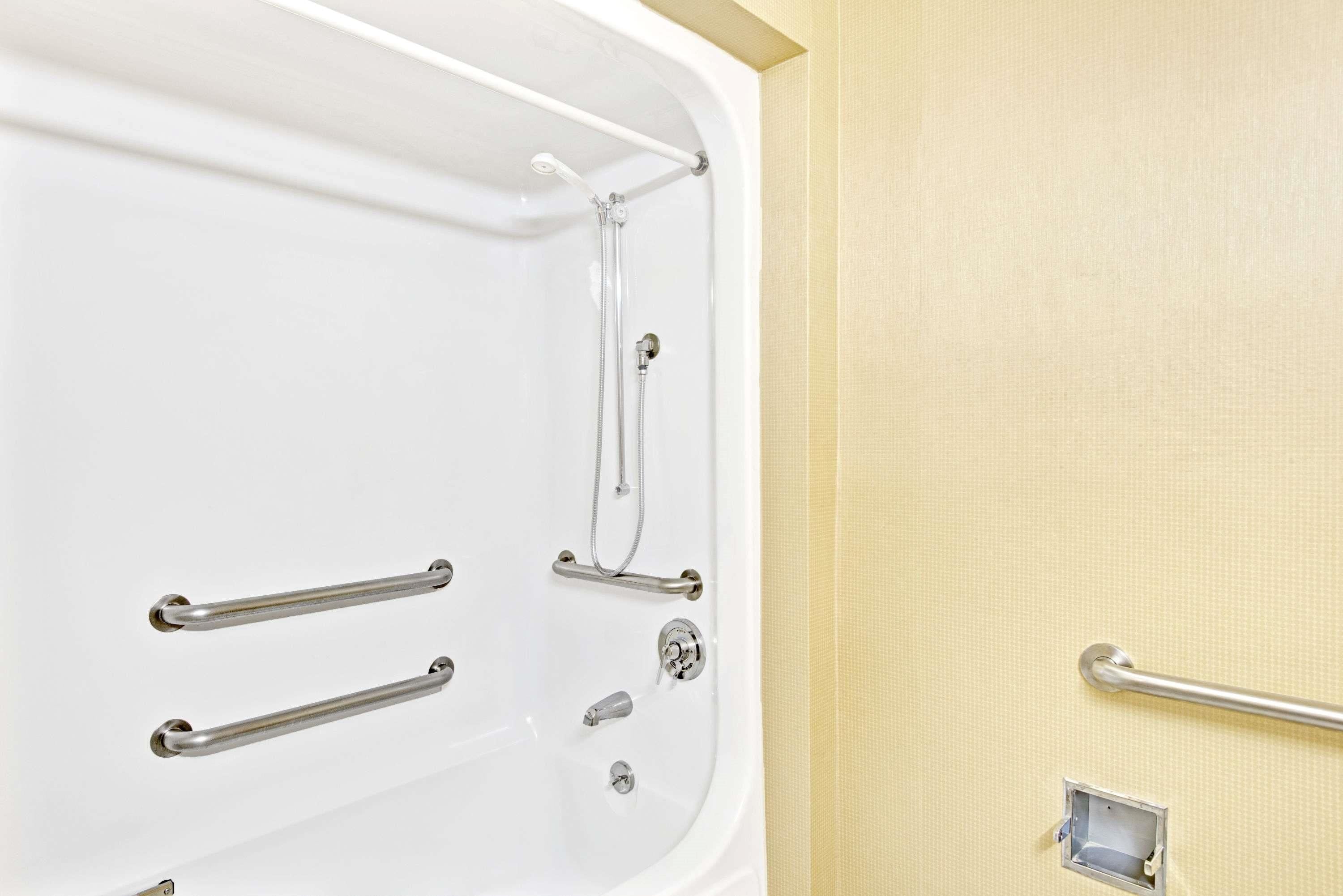 A bathroom with a white bathtub, grab bars, and a towel rack.