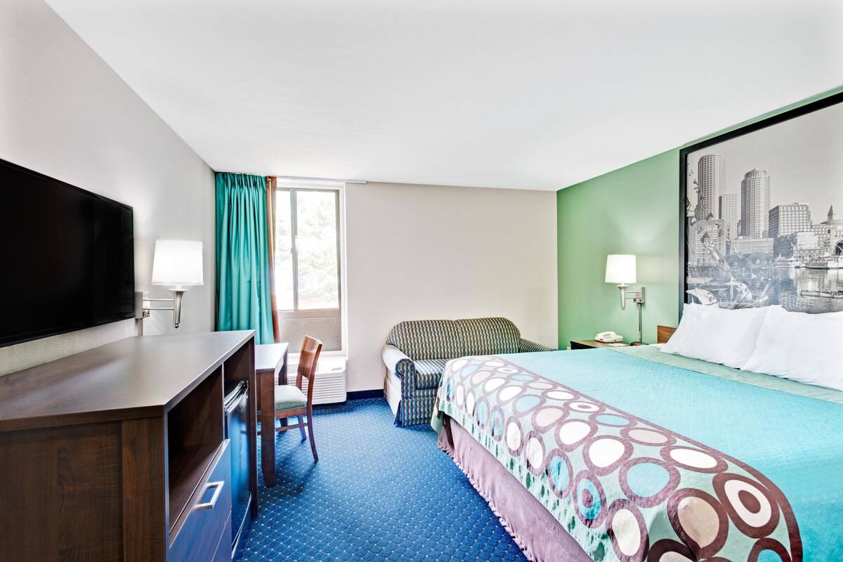 Une chambre d’hôtel avec un lit, un bureau, une chaise, une télévision et une fenêtre avec des rideaux.