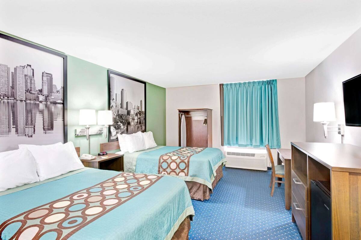 Une chambre d’hôtel avec deux lits, un bureau, une chaise, une télévision et des œuvres d’art accrochées aux murs.