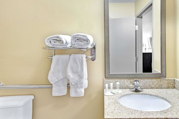 A bathroom with a toilet, a sink, and a mirror. There are towels on a rack and a towel hanging on the wall.