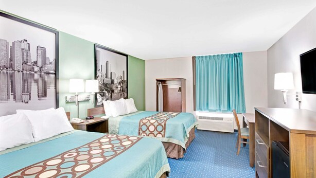 A hotel room with two beds, a desk, a chair, a TV, and a window with curtains.