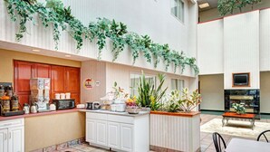 A hotel lobby with a central kitchen area, a seating area with a fireplace, and a large window overlooking the interior.