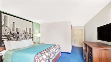 A hotel room with a bed, a desk, a television, and a cityscape painting on the wall.