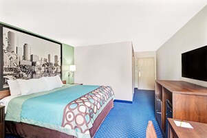 Habitación de hotel con cama, escritorio, televisor y un cuadro de un paisaje urbano en la pared.