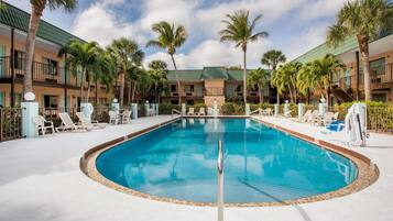 A swimming pool surrounded by lounge chairs and palm trees, with a building in the background.