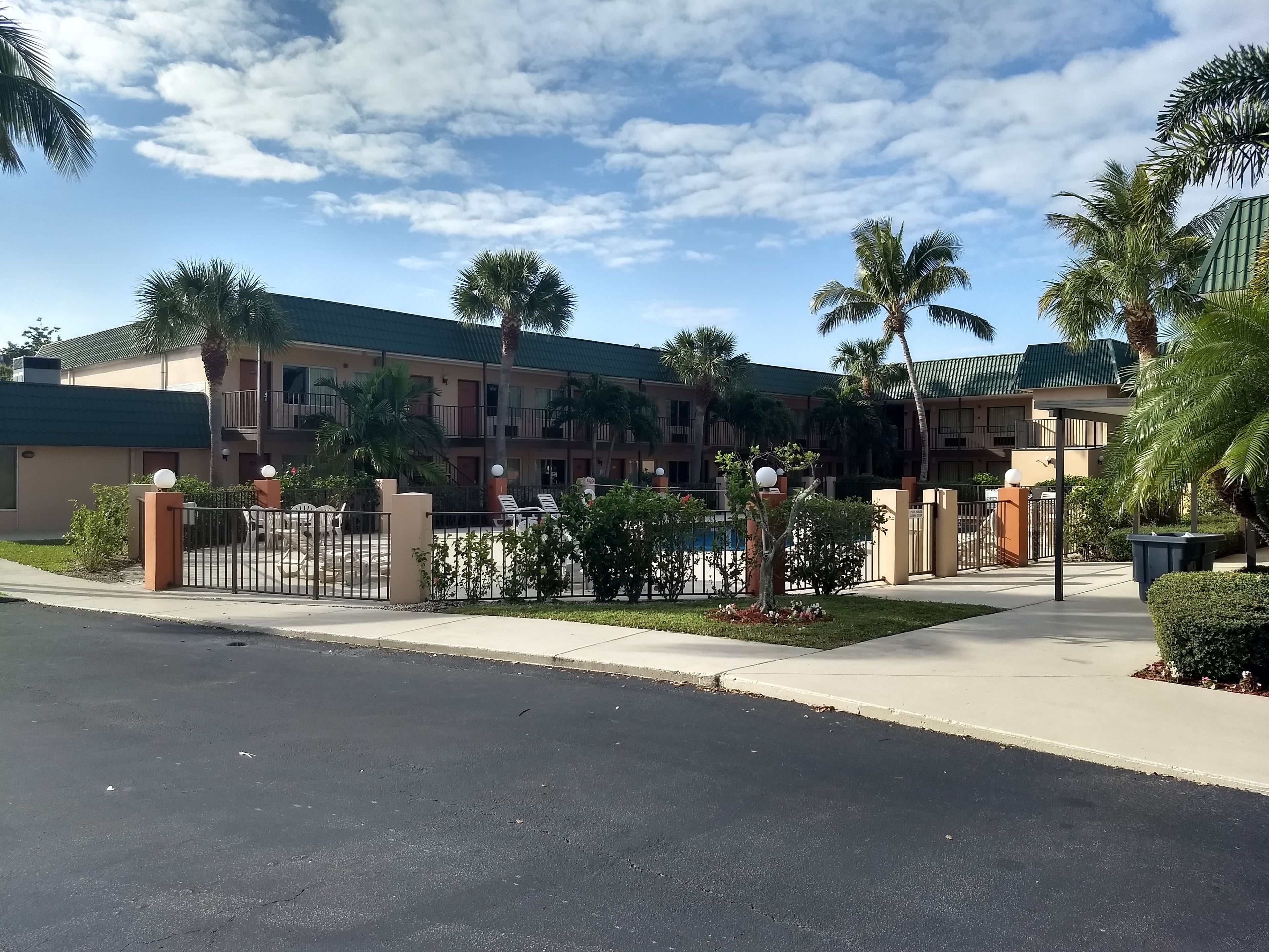 Un hotel de varios pisos con techo verde, palmeras y una entrada con portón.