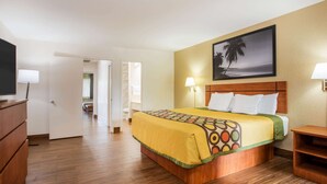 Una habitación de hotel con una cama de madera, televisión, escritorio y un cuadro con una playa.