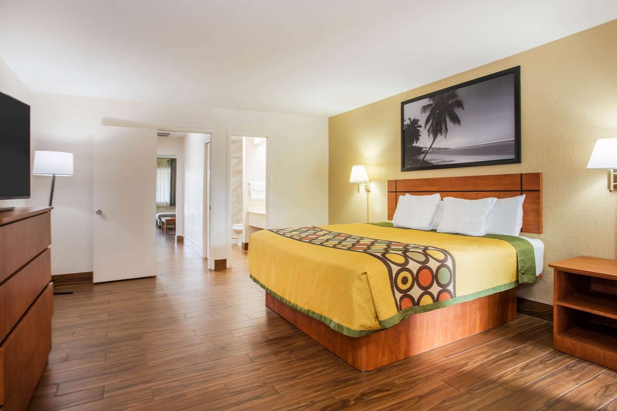 A hotel room with a wooden bed, a television, a desk, and a painting of a beach scene.