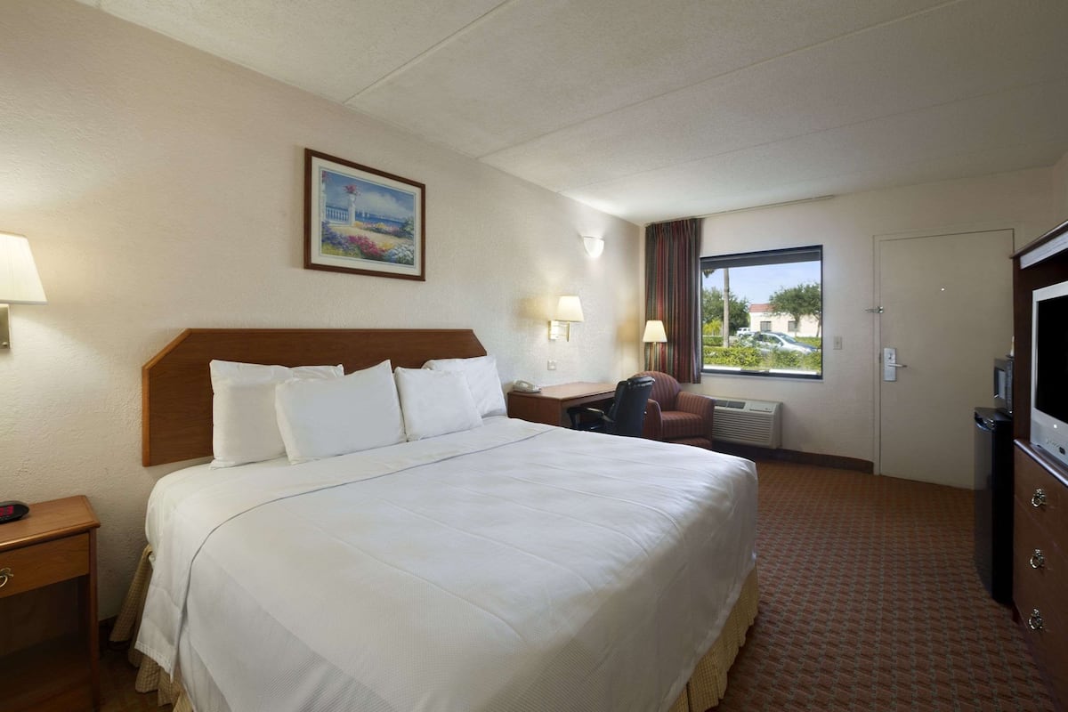 A hotel room with a large bed, a desk with a chair, a TV, and a window with curtains.