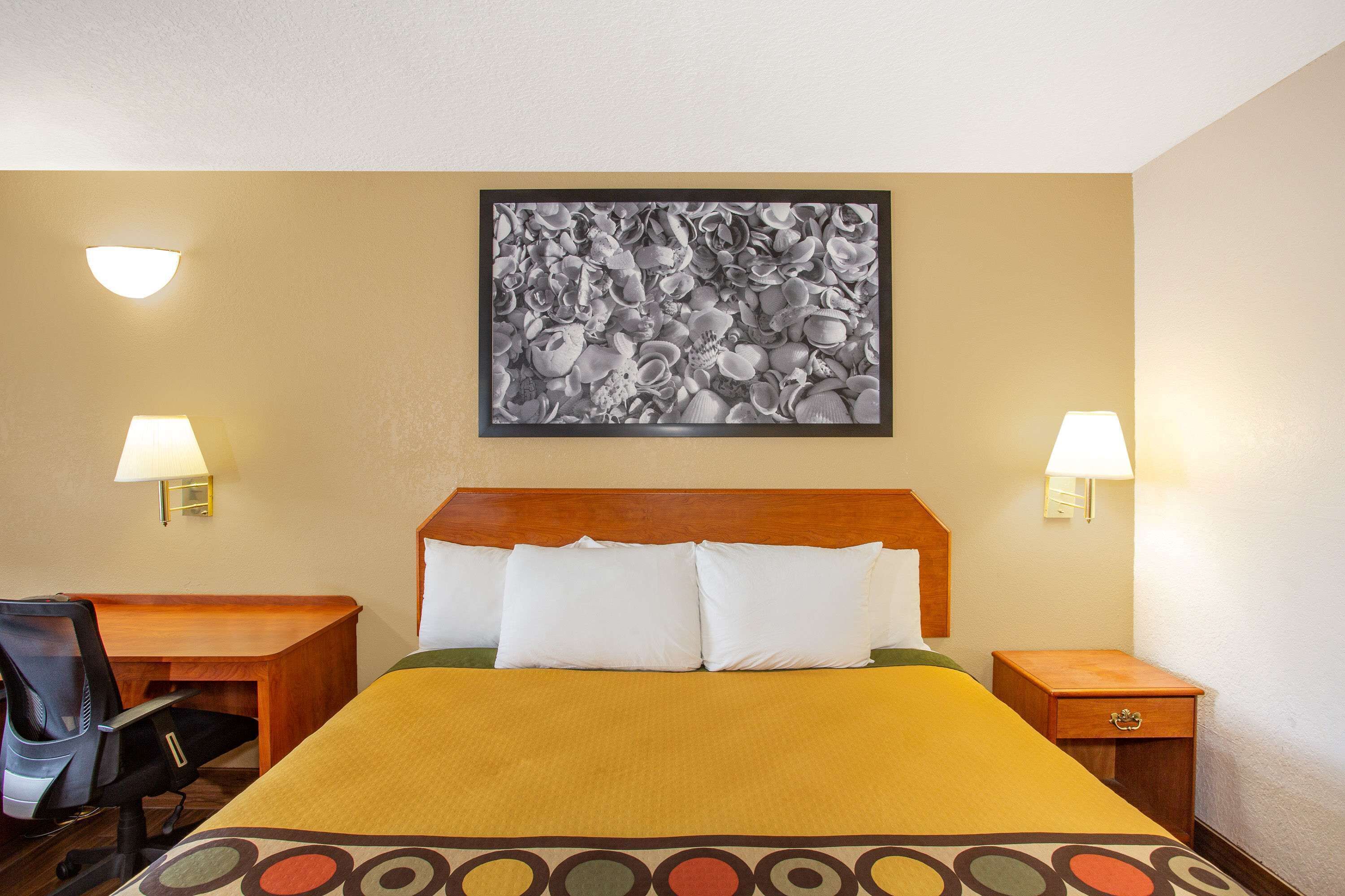 Habitación de hotel con cama, escritorio, dos sillas y dos mesitas de noche con lámparas.