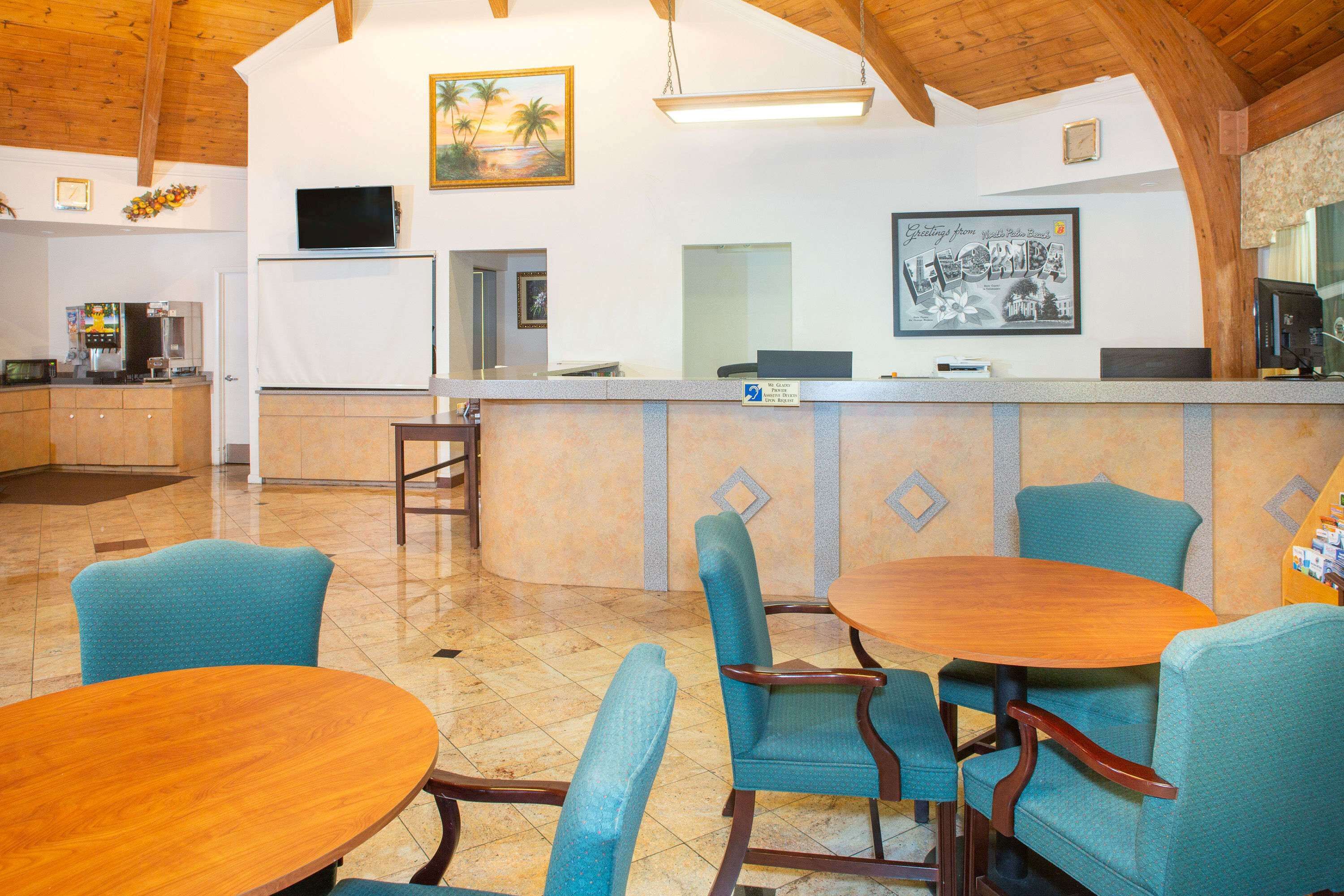 A reception area with a counter, chairs, a wooden table, and a kitchen in the background.