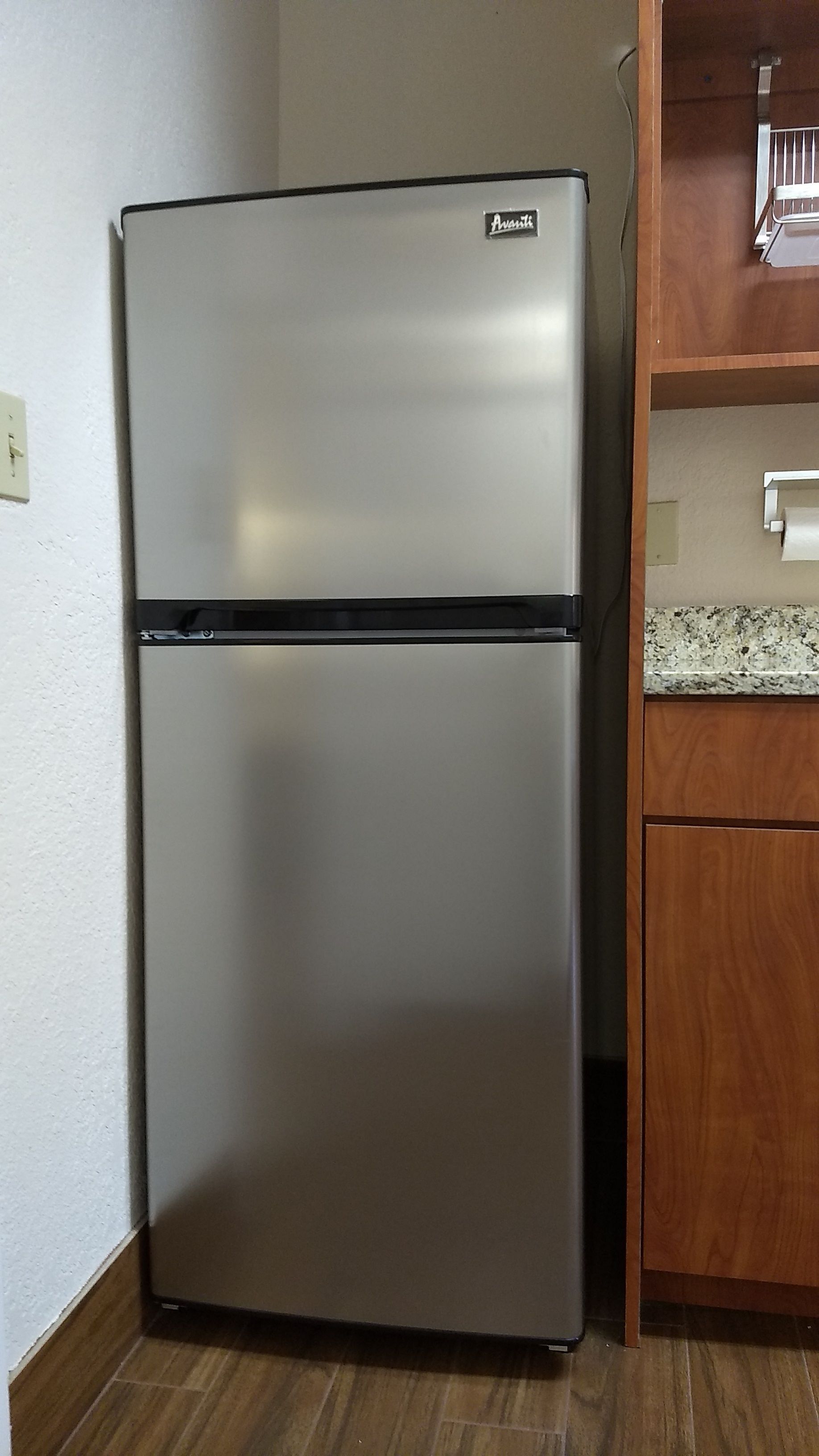 A stainless steel refrigerator with a freezer on top, located in a kitchen with wooden cabinets and a granite countertop.