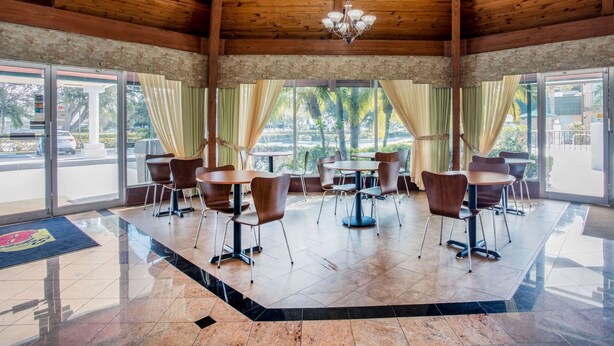 Amplio espacio interior con vigas de madera en el techo, ventanas grandes con cortinas y varias mesas y sillas dispuestas para comer o celebrar reuniones.