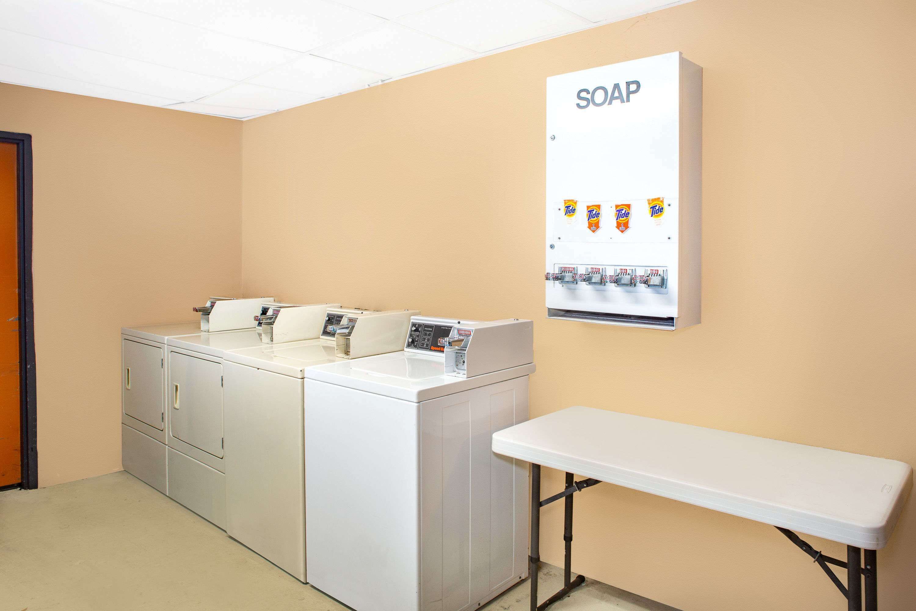Un espace buanderie comprenant un lave-linge, une table et un distributeur de savon fixé au mur.