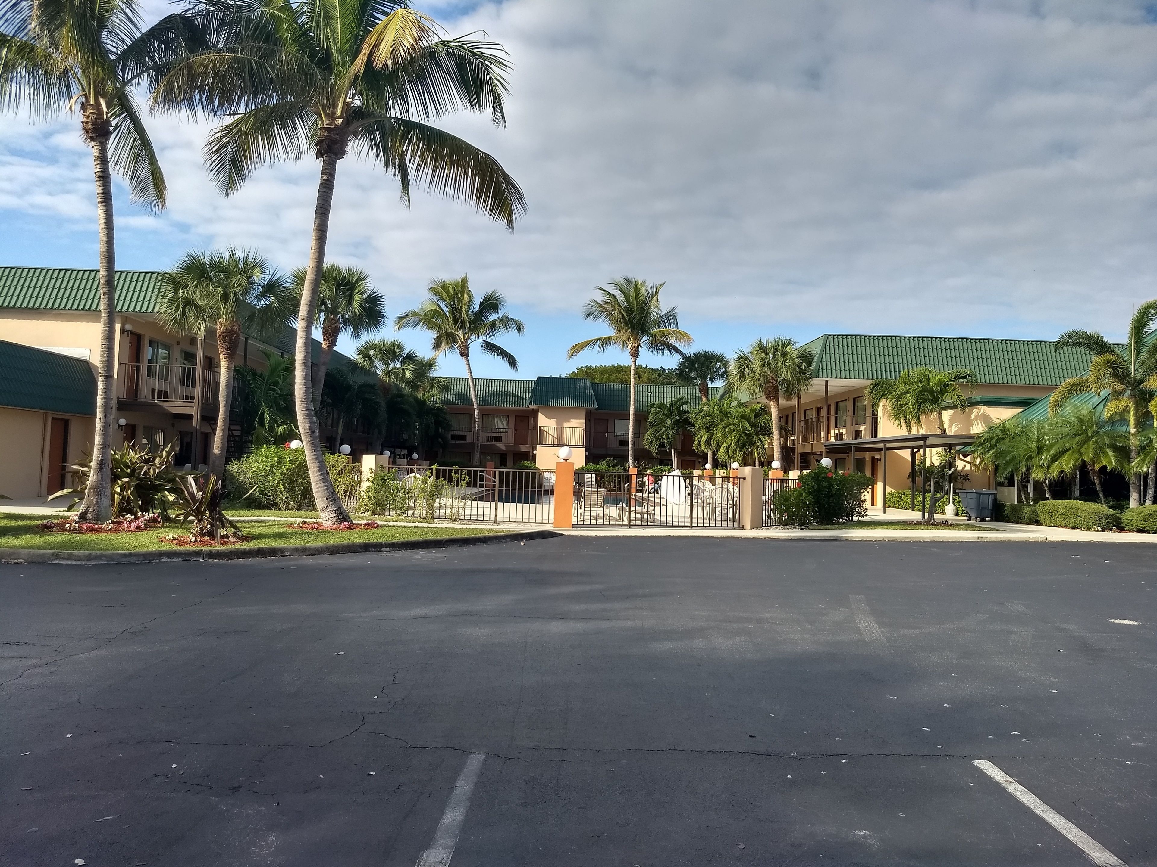 A hotel with a green roof, palm trees, and a parking lot.