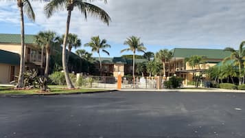 A hotel with a green roof, palm trees, and a parking lot.
