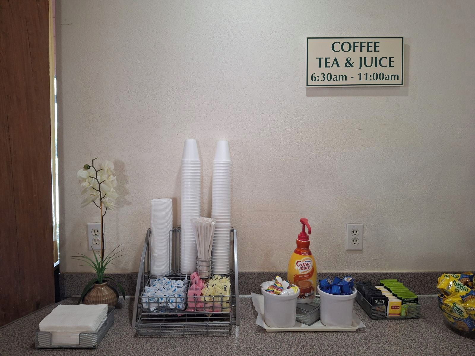 A coffee station with disposable cups, napkins, and a coffee machine, with a sign indicating availability from 6:30 am to 11:00 am.