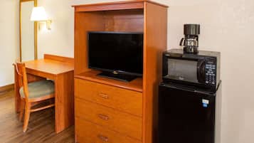 Una habitación de hotel compacta con un escritorio de madera, un televisor, un microondas y una cafetera.
