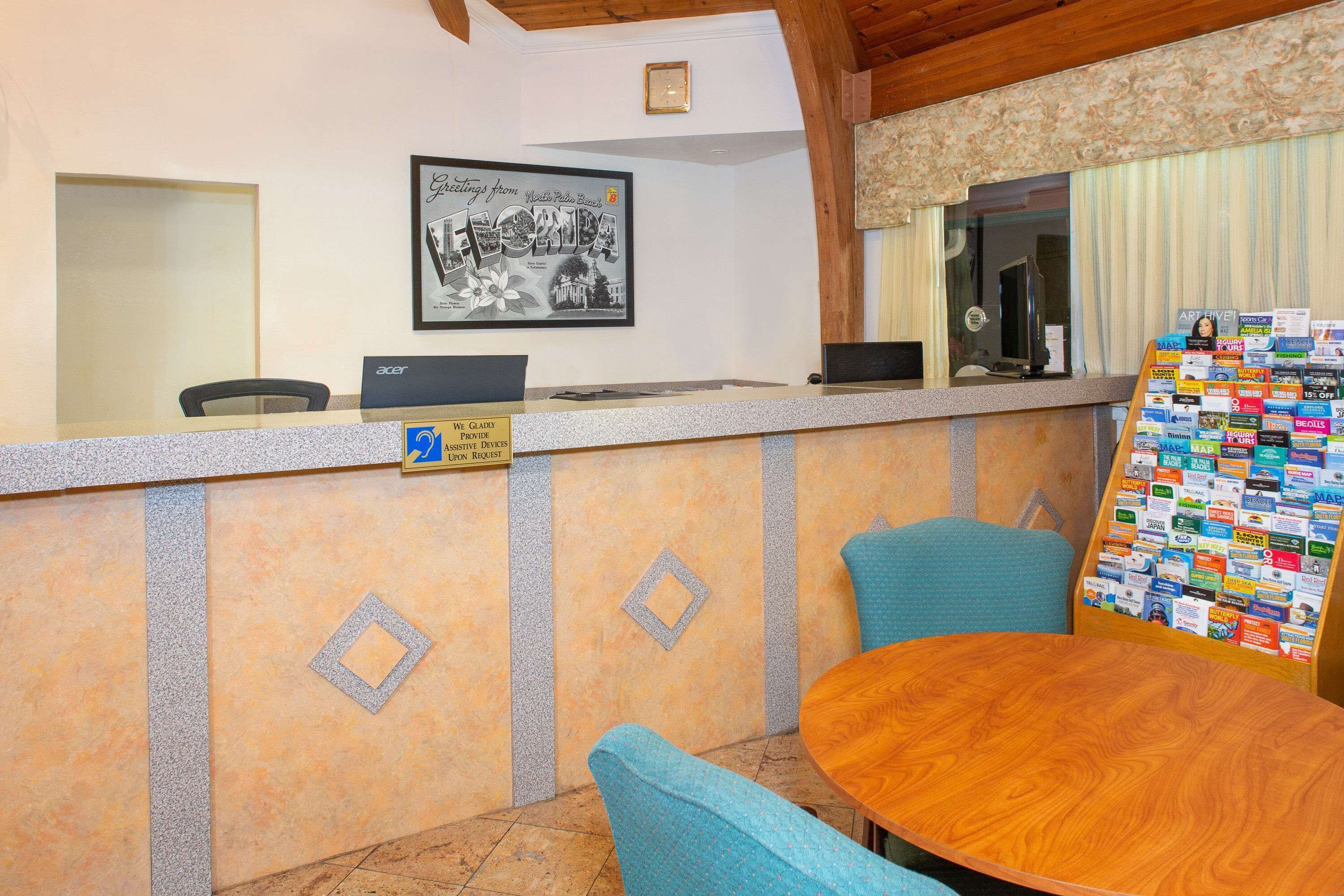 A reception area with a counter, a framed welcome sign, a computer, and a bulletin board with various notices.