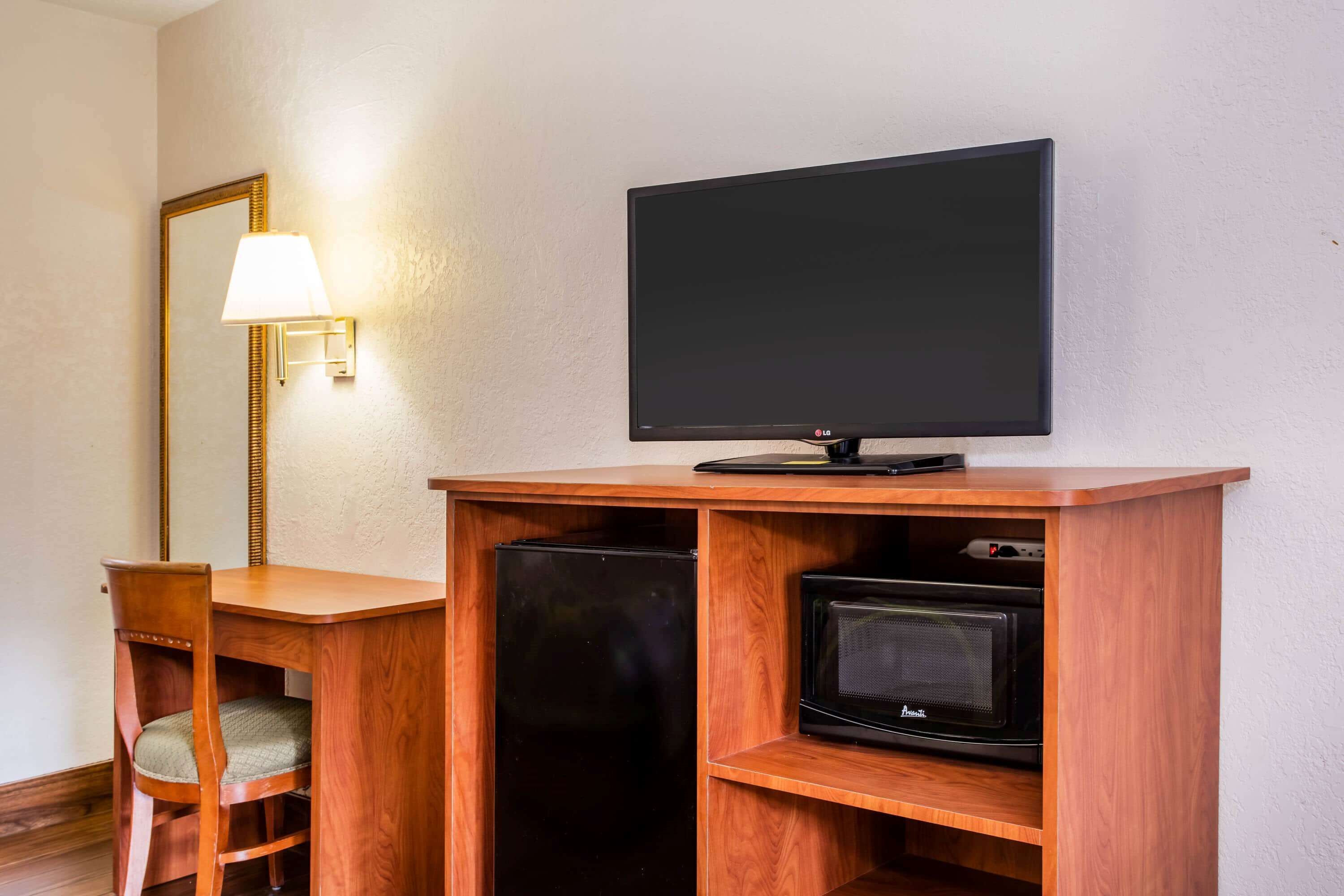 A hotel room with a wooden desk, a television, a microwave, and a mirror.