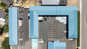 Vue aérienne d’un parking comportant de nombreuses places, d’une piscine et d’un bâtiment doté d’un toit bleu.