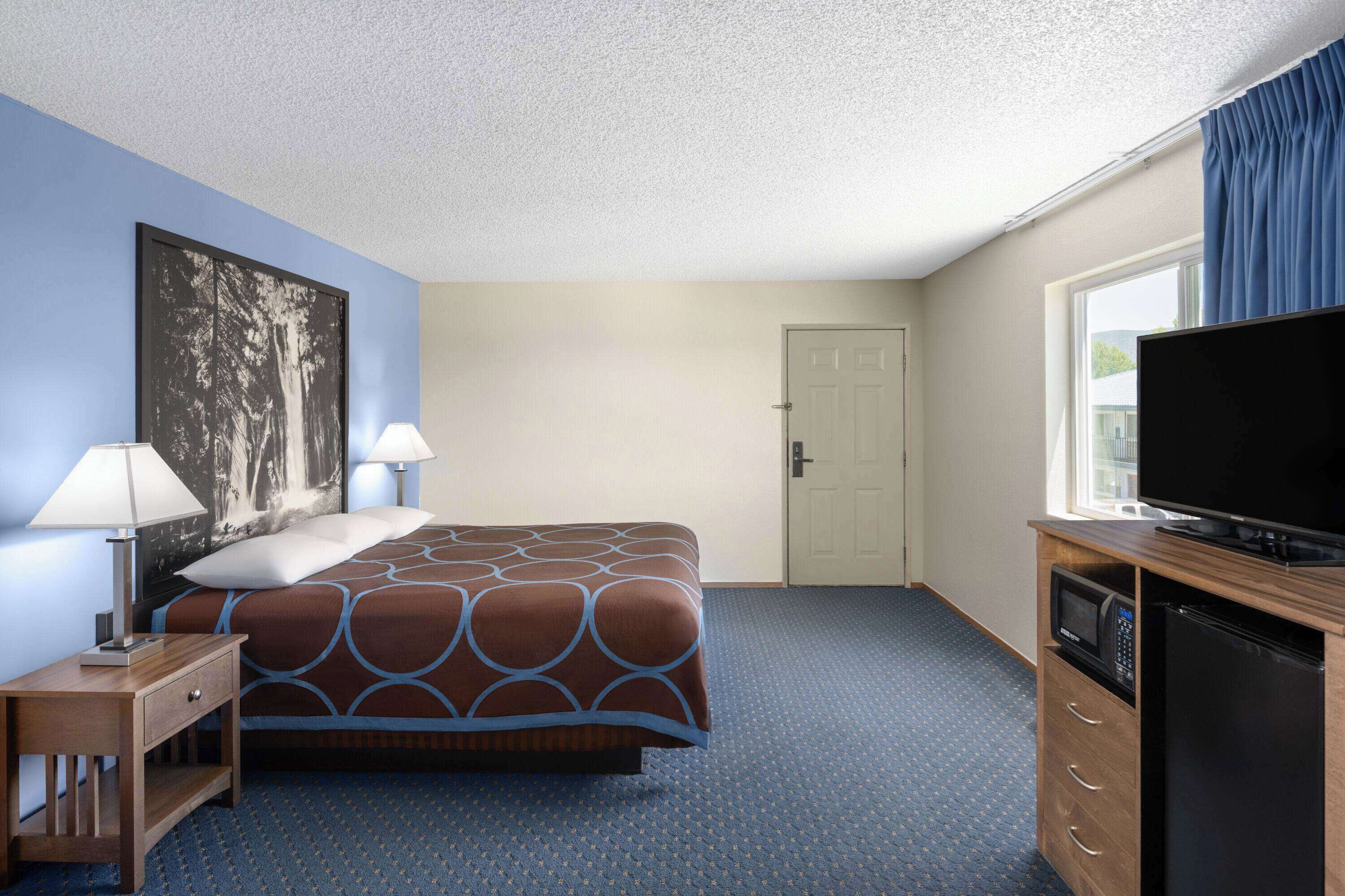 A hotel room with a bed, two bedside lamps, a flat-screen TV, a microwave, and a refrigerator.
