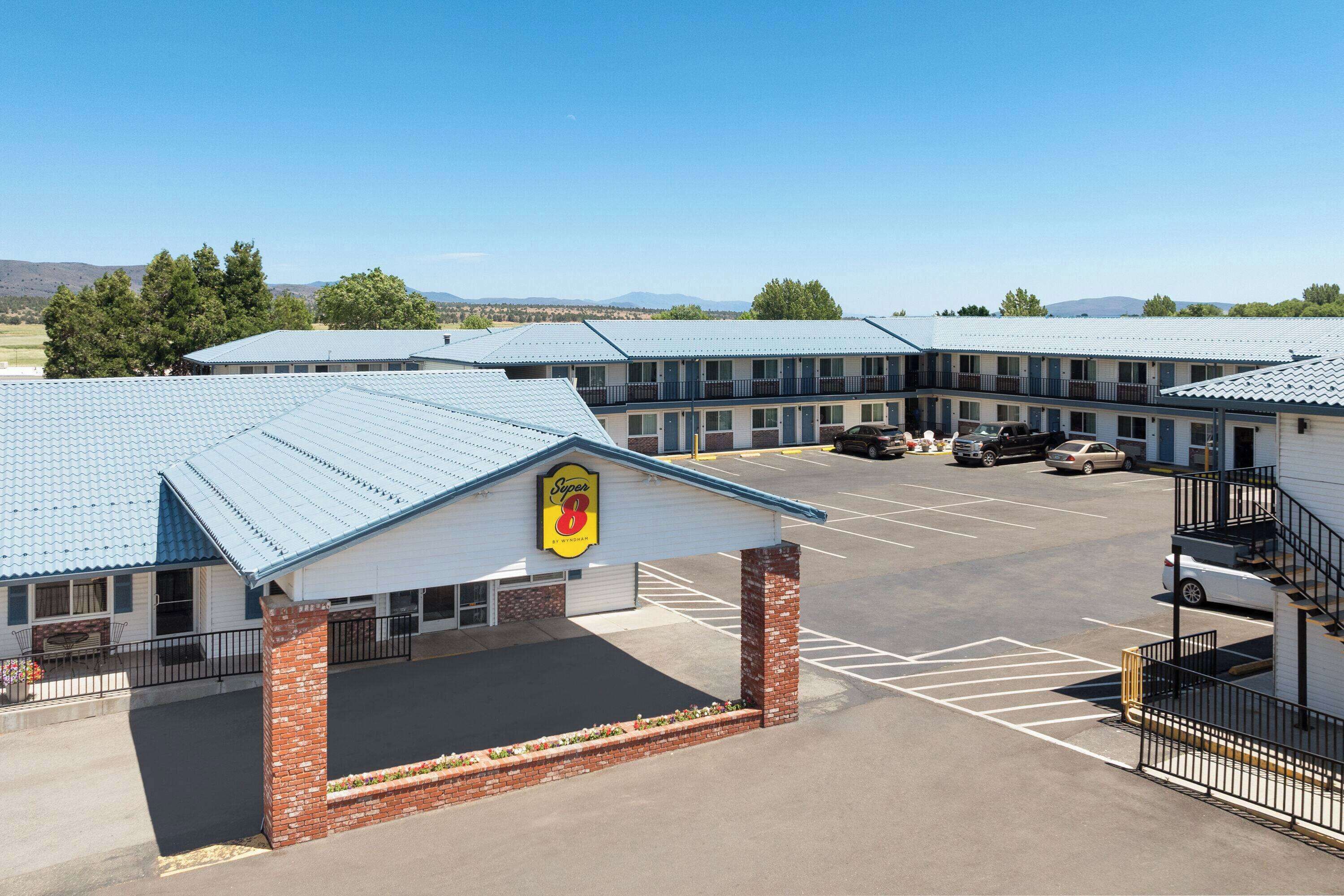 A motel with a blue roof, a parking lot, and a sign with a yellow and red logo.