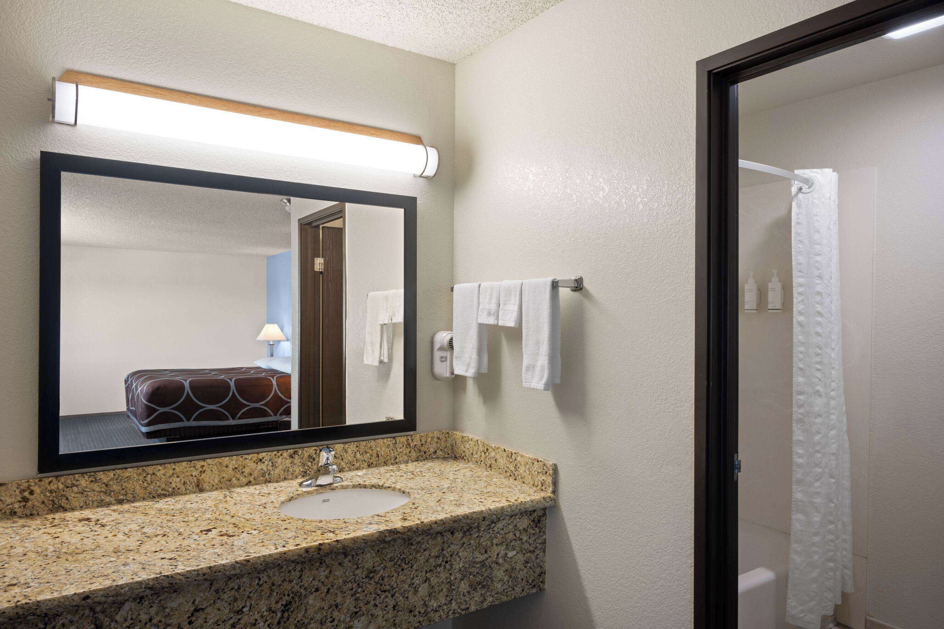 A bathroom with a granite countertop sink, a mirror, a towel rack, and a shower curtain.