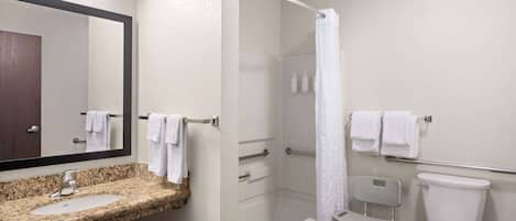 Un baño con lavamanos de encimera de granito, espejo, ducha con puerta de vidrio, inodoro y barra de apoyo.