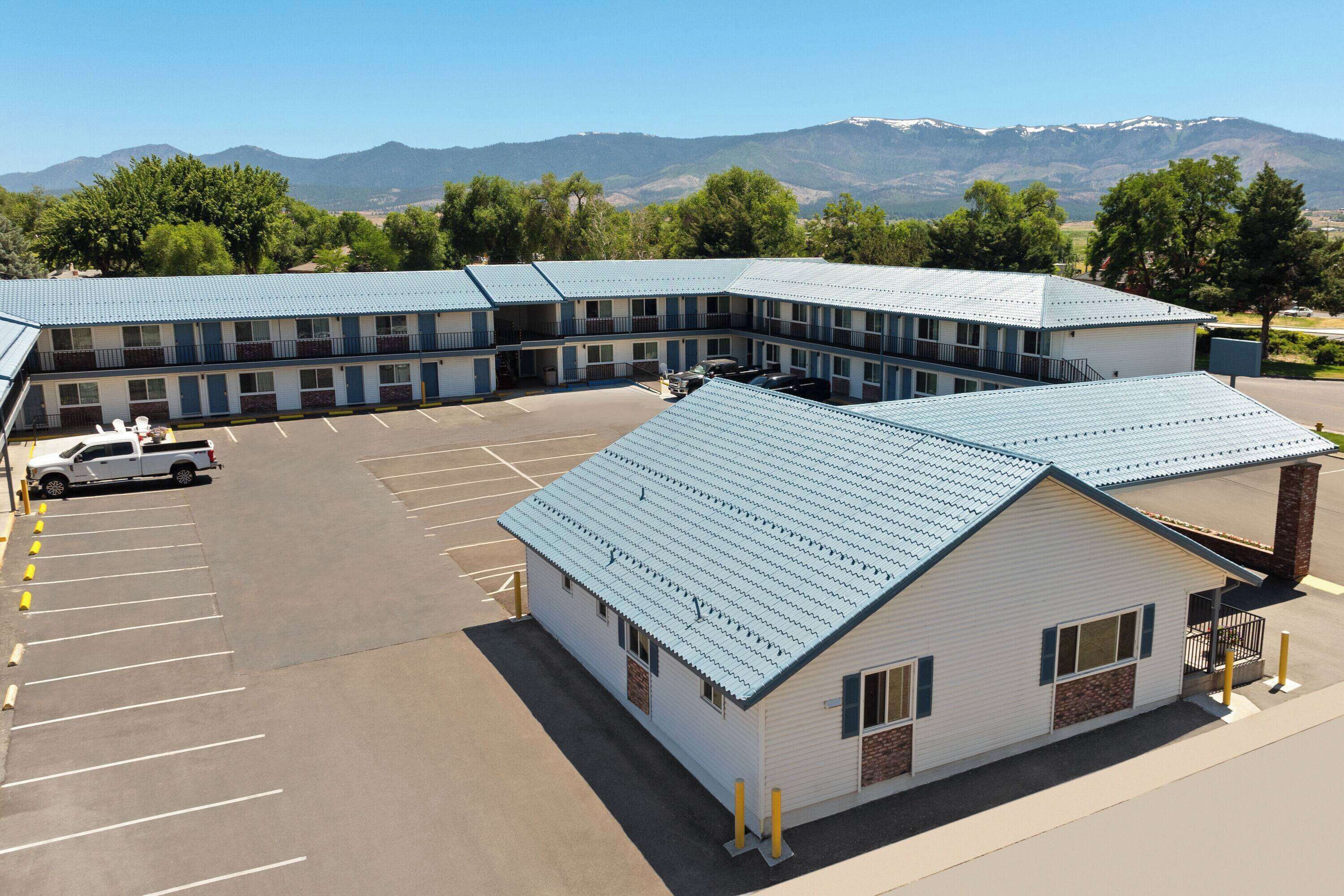 A motel with a parking lot and a mountain backdrop.