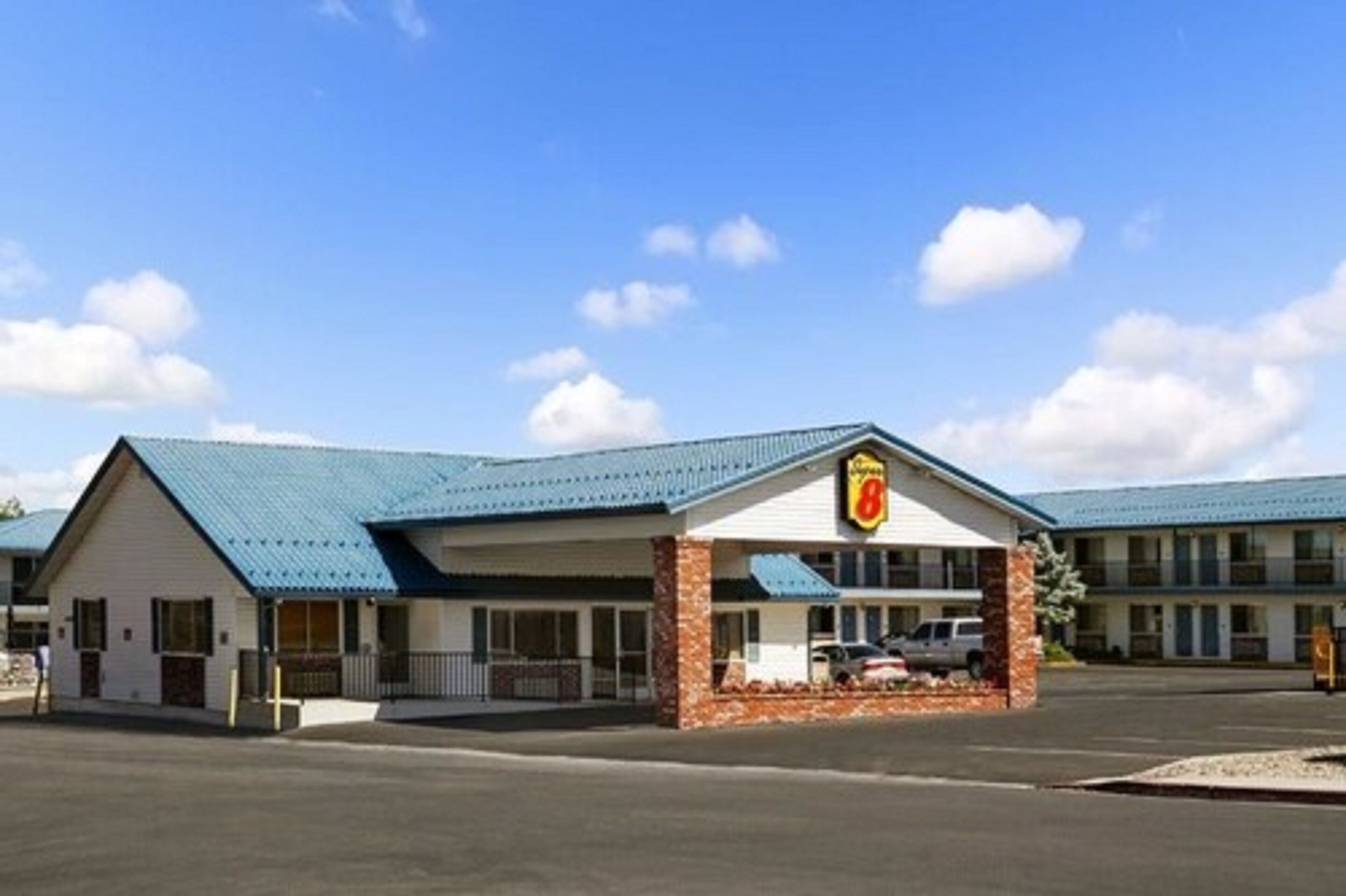 A motel with a blue roof, a central entrance, and a parking lot.