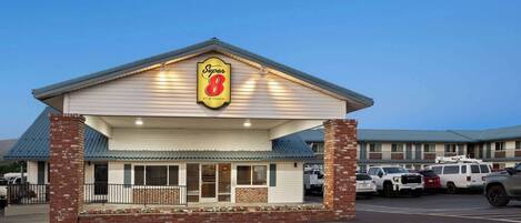 Un motel Super 8 con fachada de ladrillo, un acceso cubierto y un estacionamiento con varios vehículos.