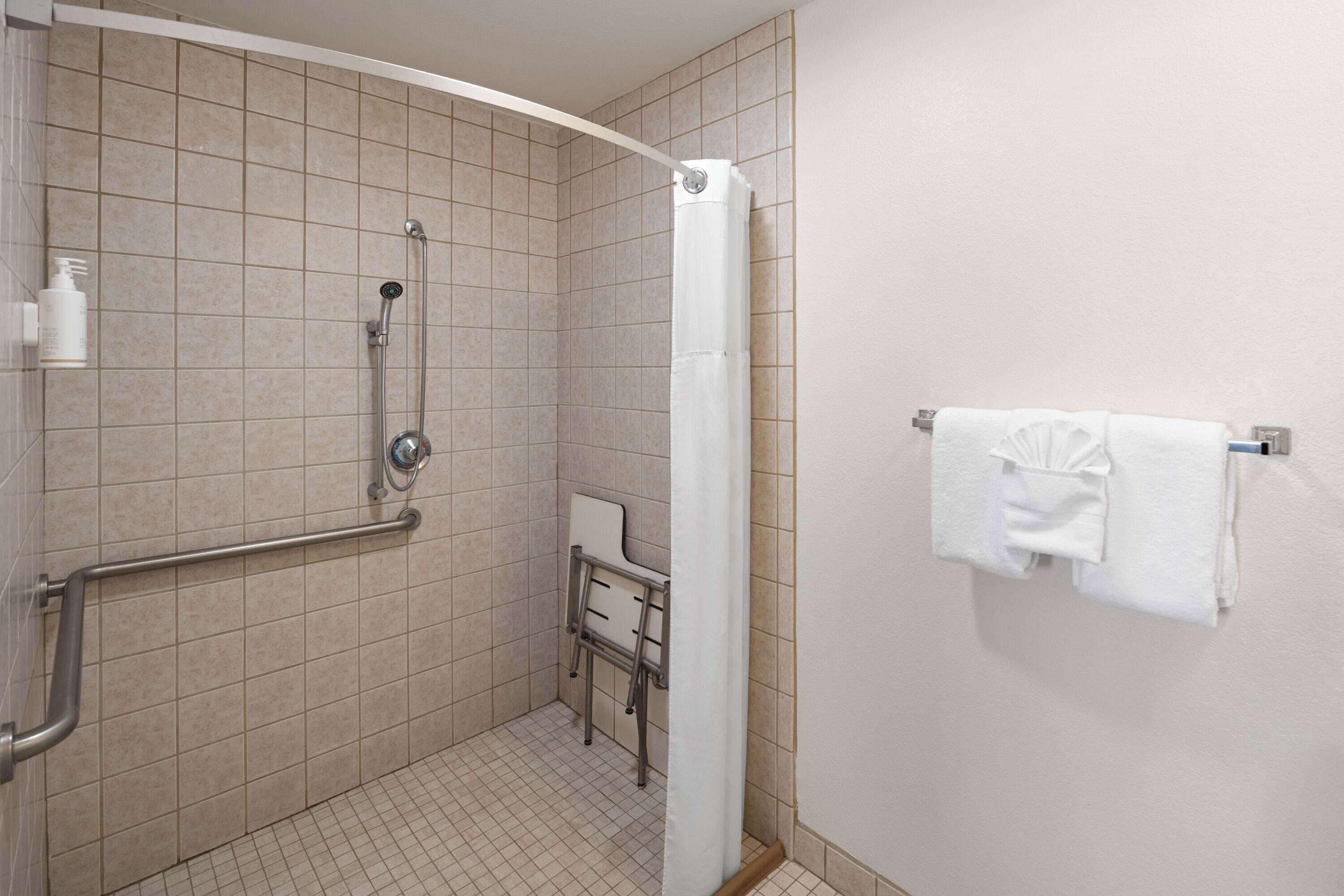 A shower with a grab bar, a white towel rack, and a small bench.