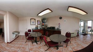 Un petit coin repas avec une petite cuisine, un réfrigérateur, un four à micro-ondes et un téléviseur. Quatre chaises sont disposées autour d’une table ronde.
