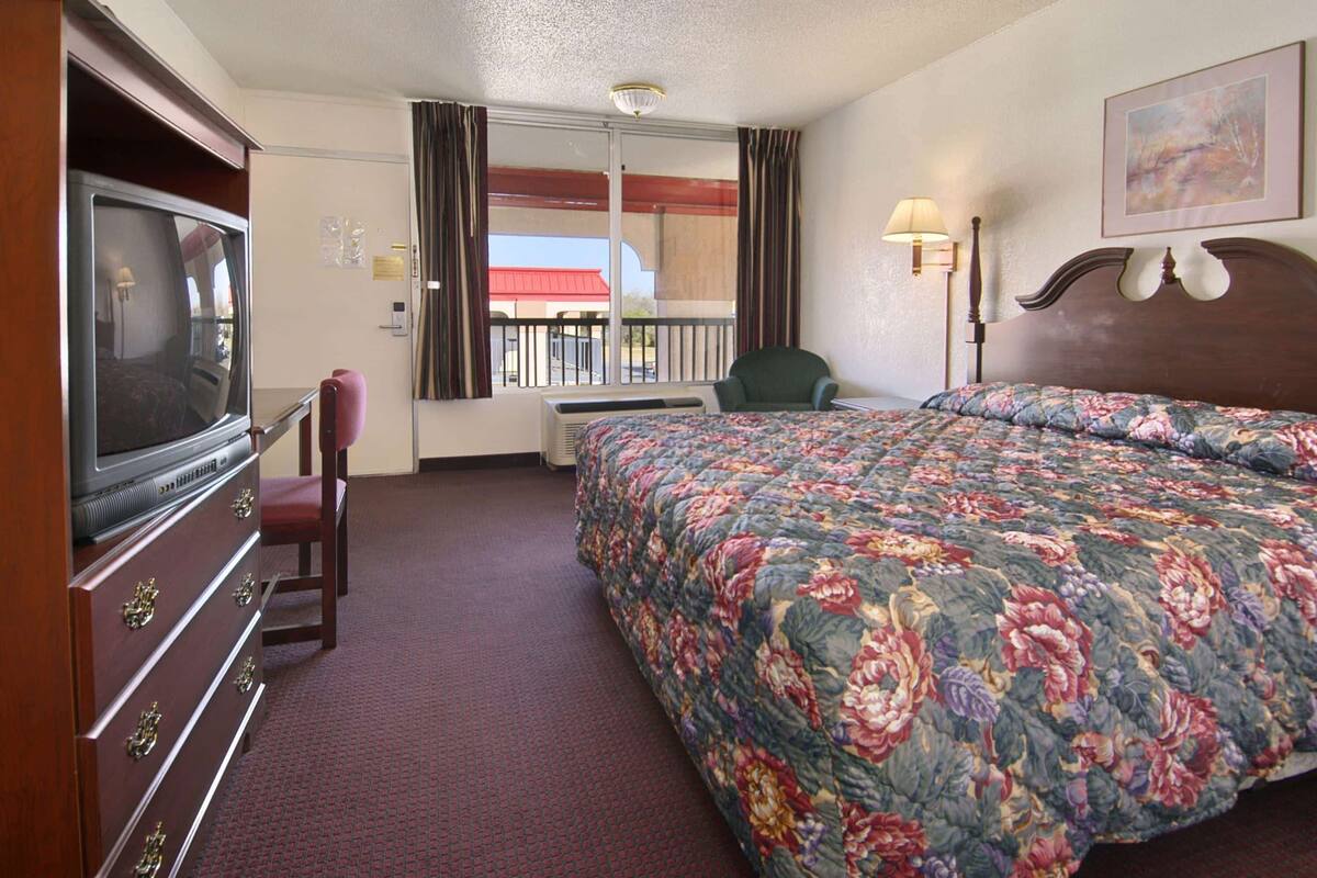 Ein Hotelzimmer mit einem großen Bett, einem Fernseher, einem Sessel und einem Fenster mit Vorhängen.