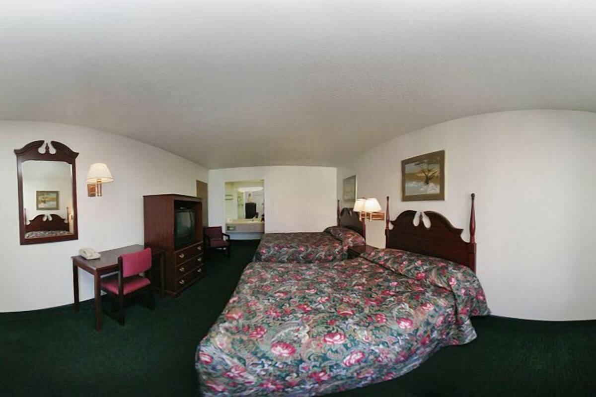 Ein Hotelzimmer mit Bett, Schreibtisch, Stuhl, Fernseher, Spiegel, Lampe und Fenster.