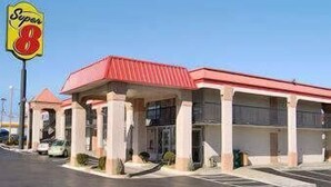 Un motel de type Super 8, avec un toit rouge et des colonnes blanches, comprenant un parking et surplombant un ciel d’un bleu limpide.