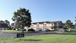 A Harmony Hotel with a parking lot, a grassy area, and a building with multiple floors.