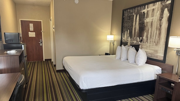 A hotel room with a large bed, a desk with a computer, a TV, and a painting on the wall.