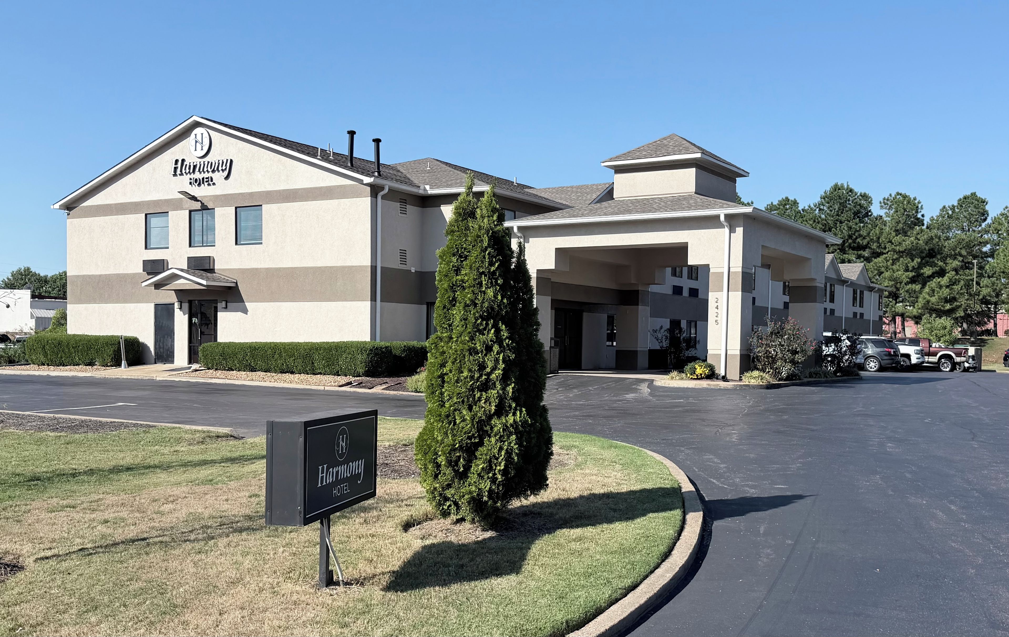 A Harmony Hotel with a modern design, featuring a two-story building with a covered entrance and a parking lot.