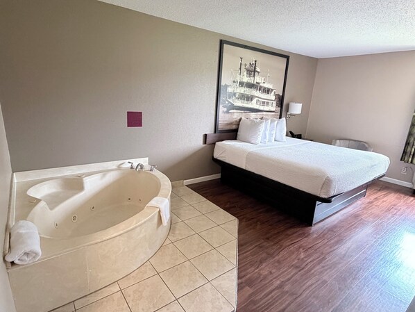 A hotel room with a large bathtub, a bed with white bedding, and a framed picture on the wall.