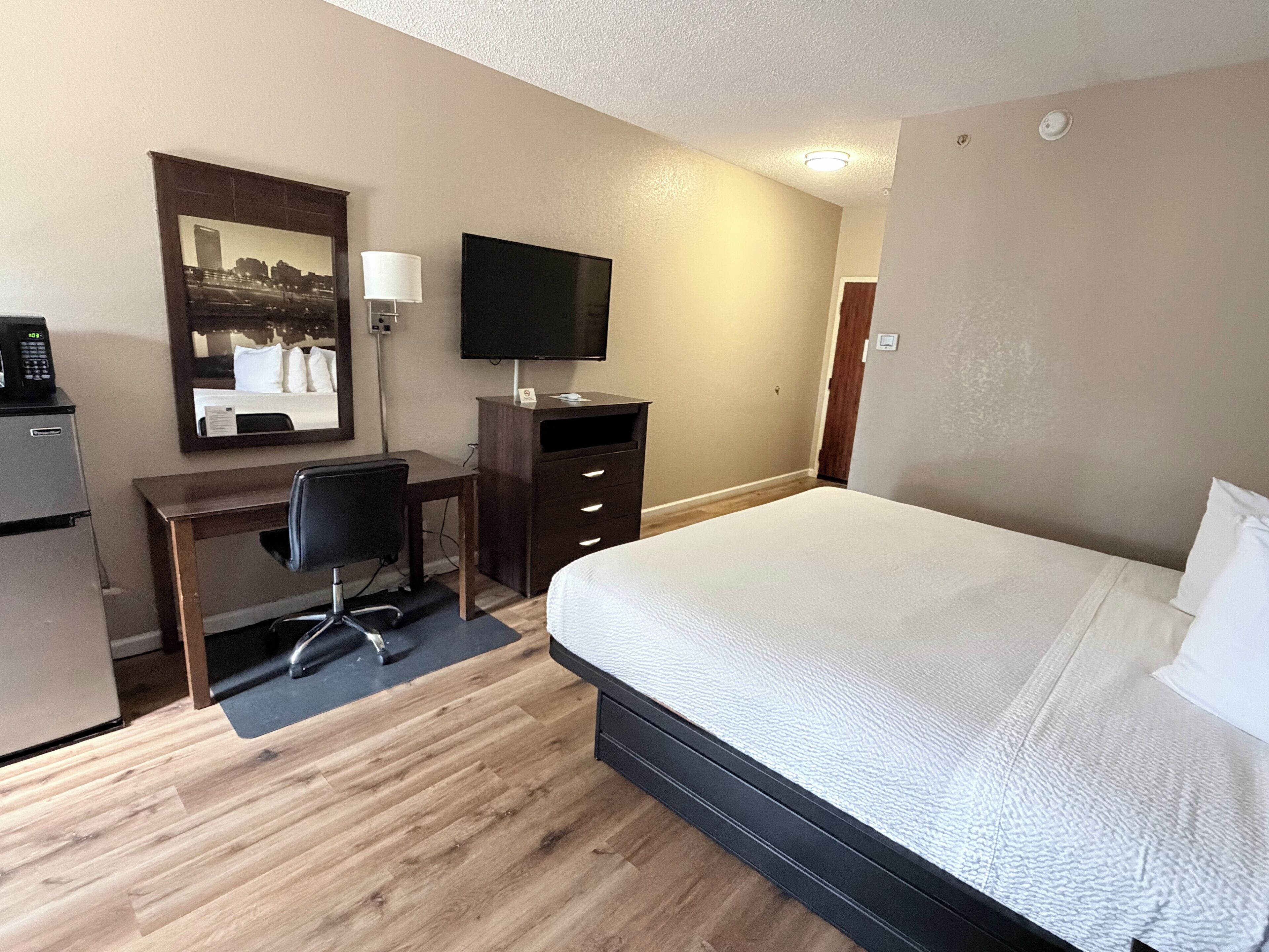 A hotel room with a bed, desk, chair, television, and a mirror.